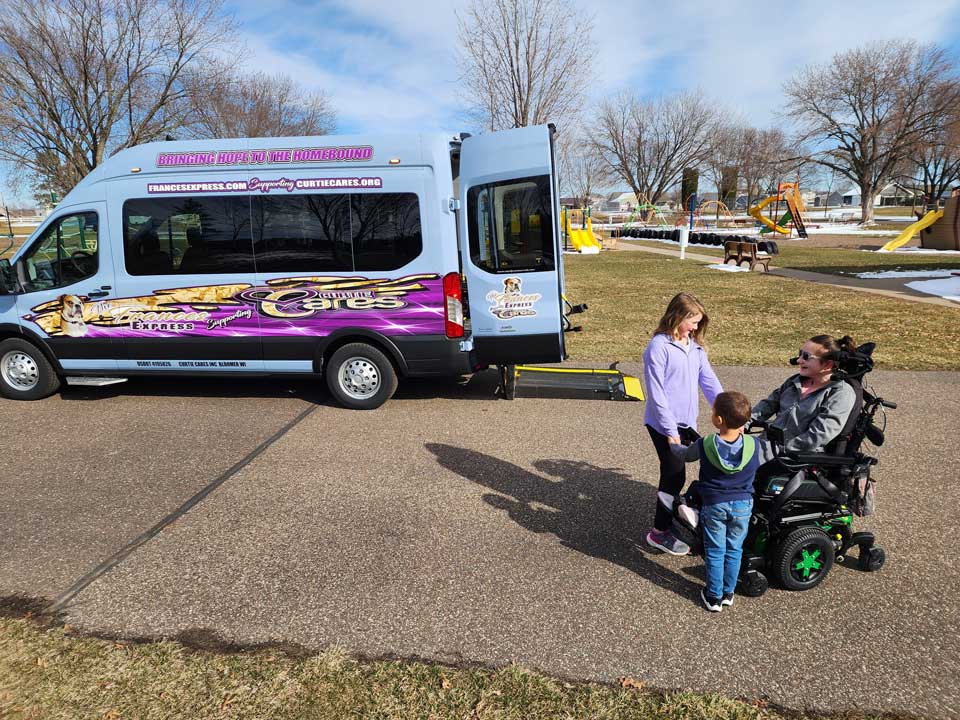 Woman sitting in wheelchair talking to kids. Frances Express van in background.